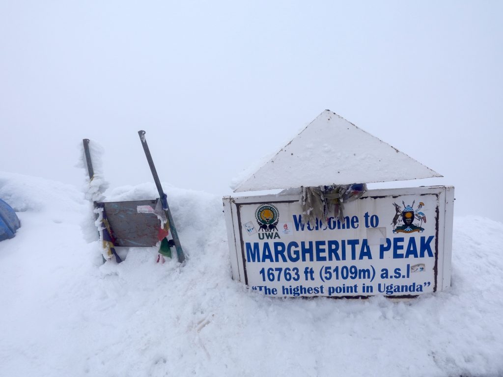 Climber celebrating at the summit of Margherita Peak after using ice axe and crampon rental in Kampala